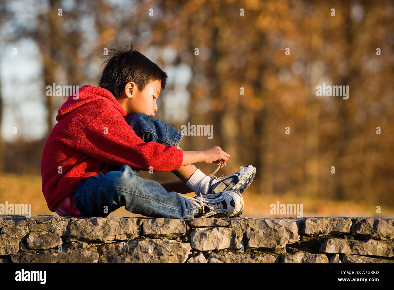 Asian boy on wall tying shoe, Tennessee Stock Photo