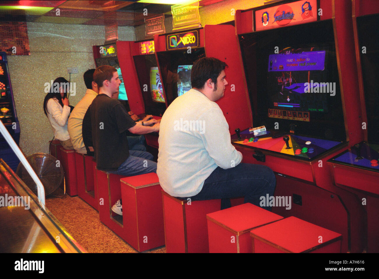 Young people playing on the games machines in amusement arcade. Stock Photo