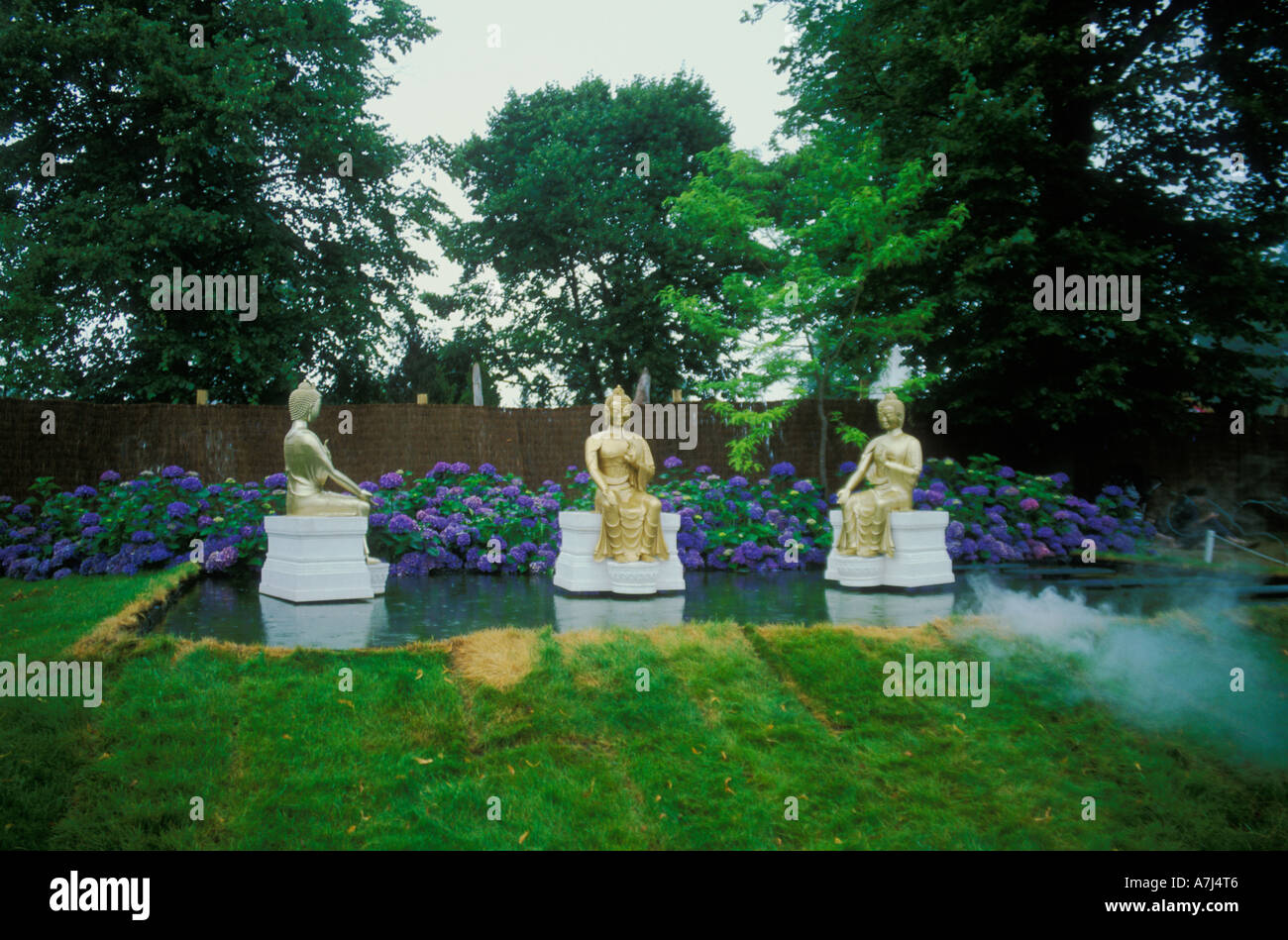 Garden design with three floating Buddha statues with hydrangea bush behind, Amnesty International Garden at Hampton Court Stock Photo