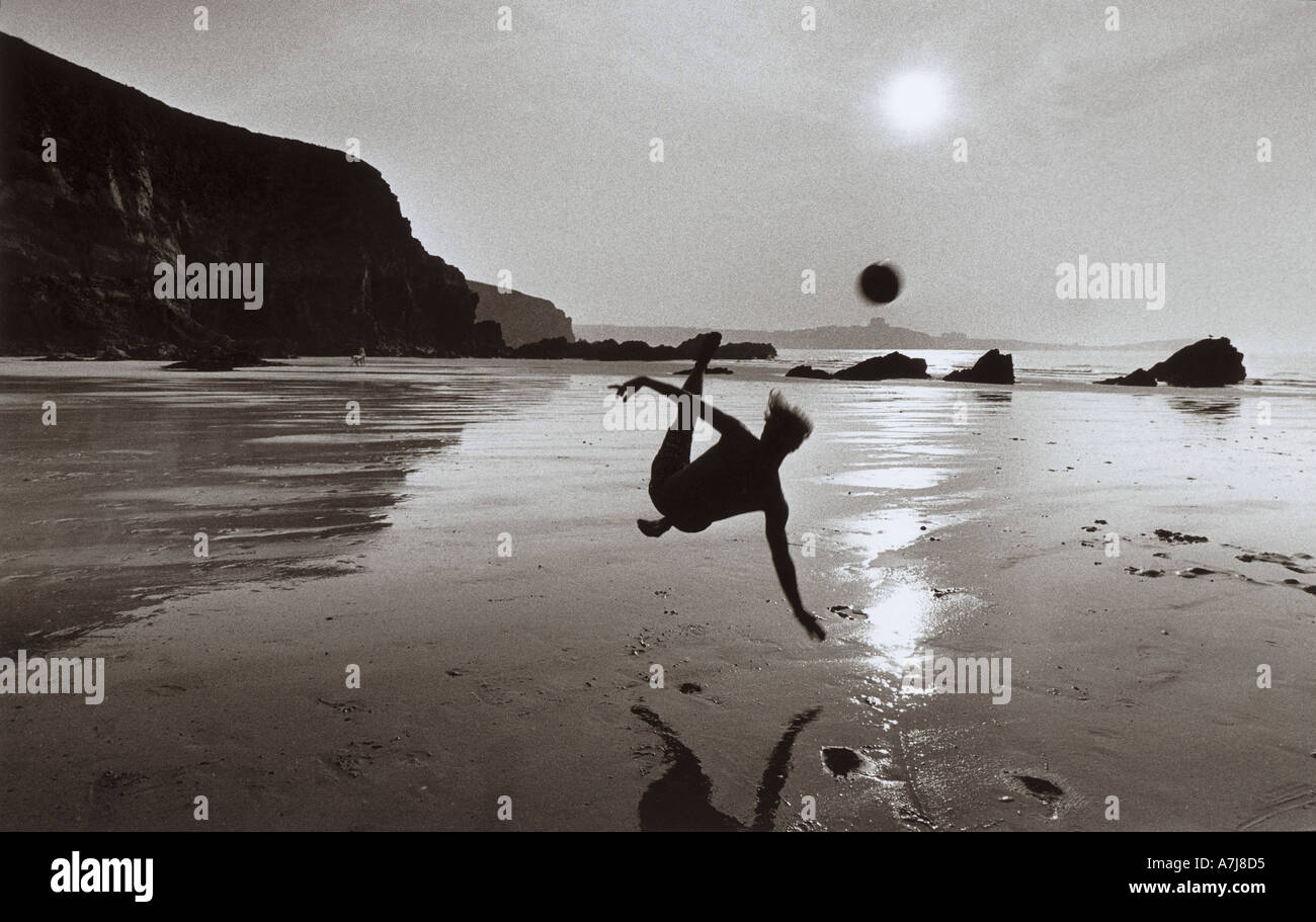 A boy plays a last game of beach football at sunset on Lusty Glaze beach Newquay Cornwall Stock Photo