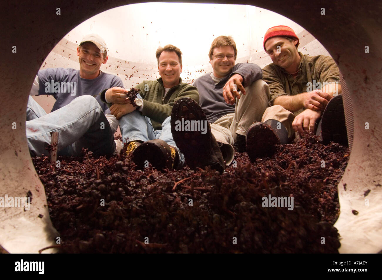 Joe Dobbes holding grape cluster with his winemaking crew pose for a portrait inside a fermentation tank at his winery Dundee Or Stock Photo