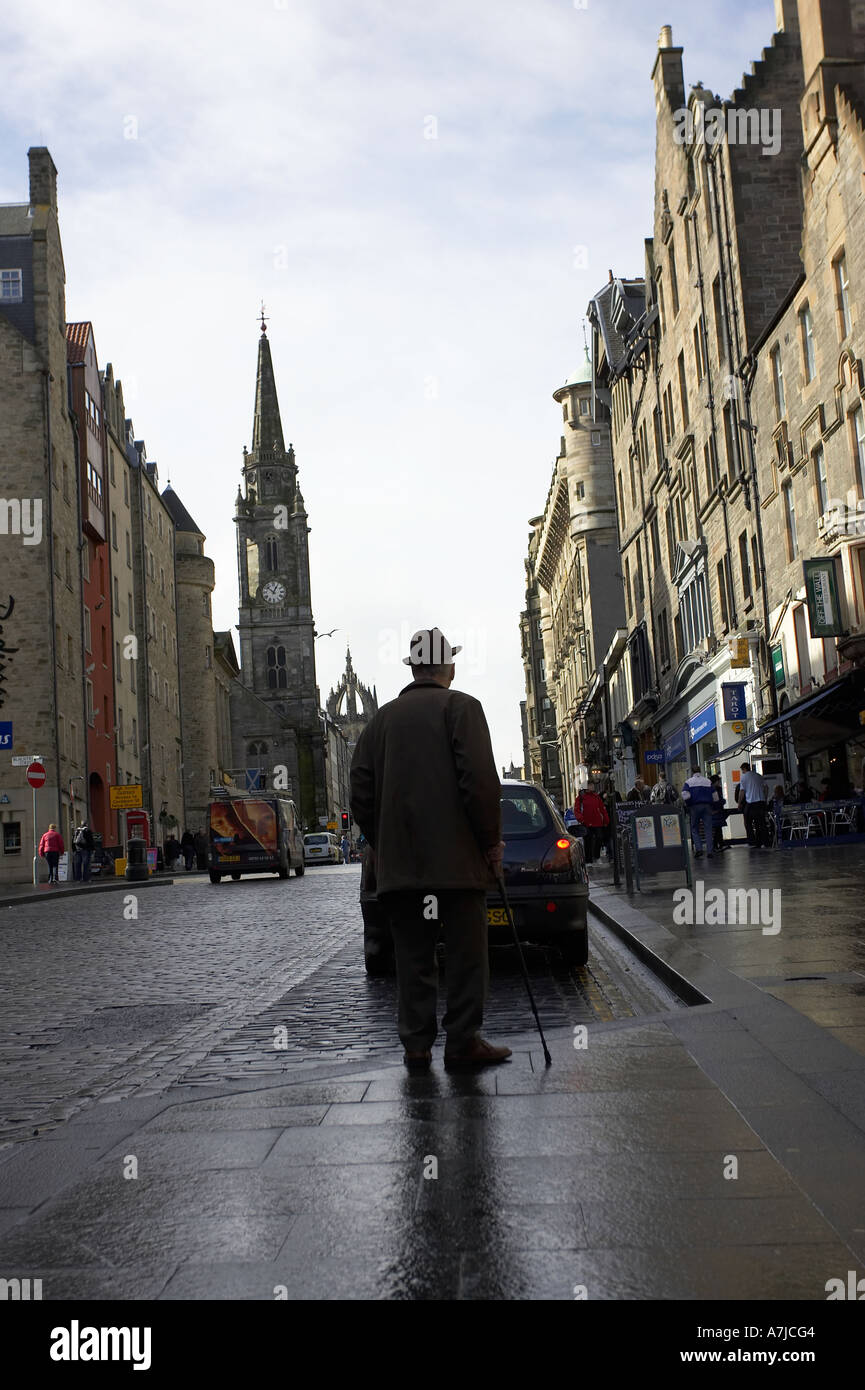 old elderly man in long coat hat and with a walking stick on wet pavement with reflection the royal mile Stock Photo