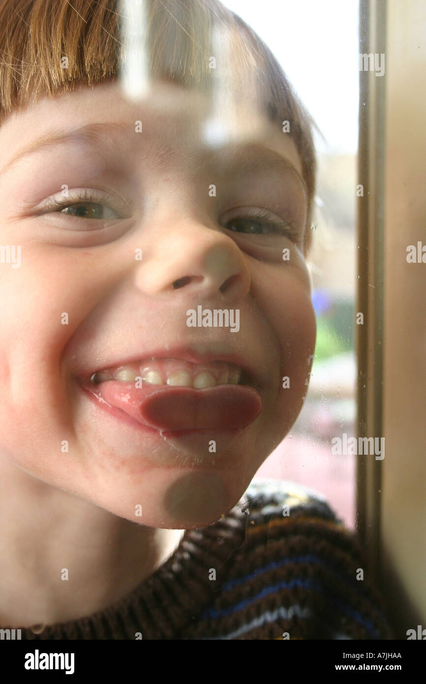 boy-smiling-and-sticking-out-tongue-against-glass-door-A7JHAA.jpg
