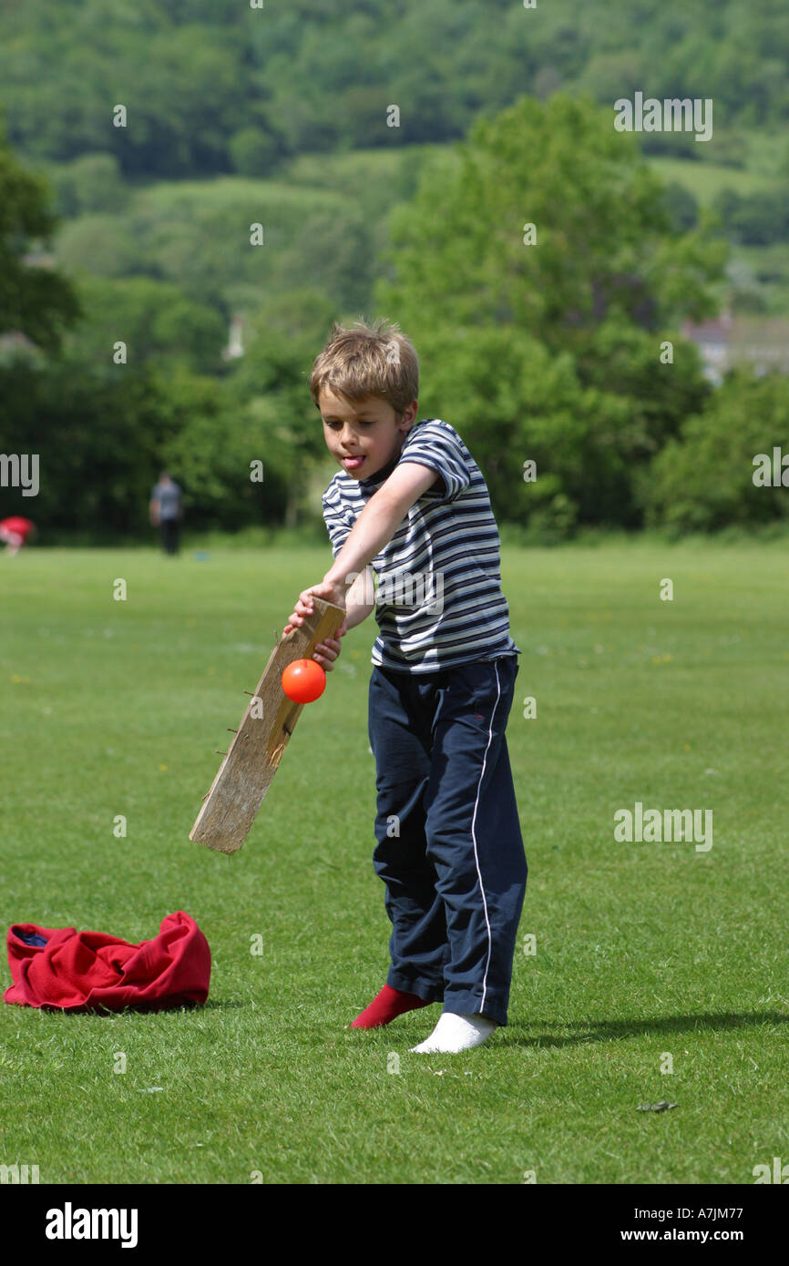 Young boy plays cricket with an improvised chunk of old wood as a bat in the local park Stock Photo