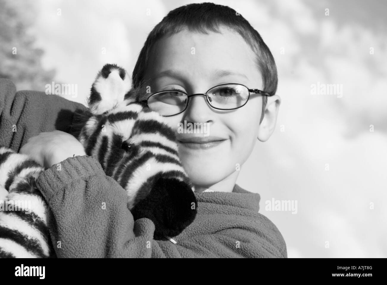 B W young boy wearing glasses smiling hugging a stuffed zebra doll Stock Photo