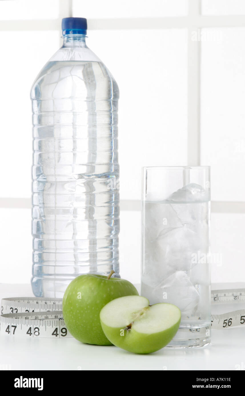 PORTRAIT SHOT OF A BOTTLE OF WATER WITH A GLASS OF WATER AND TWO APPLES ONE WHOLE AND ONE CUT IN HALF WITH MEASURING TAPE Stock Photo