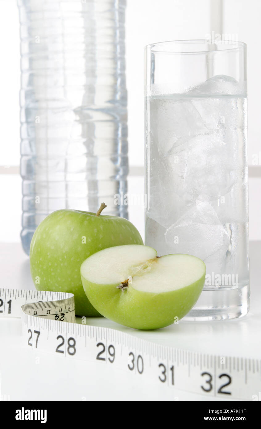 PORTRAIT SHOT OF A BOTTLE OF WATER WITH A GLASS OF WATER AND TWO APPLES ONE WHOLE AND ONE CUT IN HALF WITH MEASURING TAPE Stock Photo