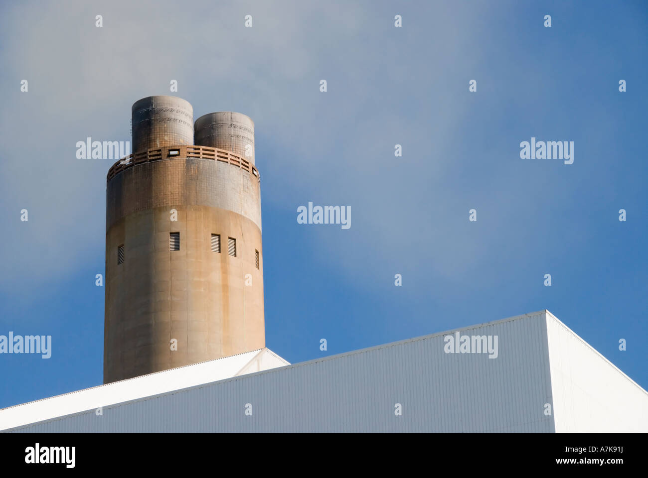 A smoking  power  station chimney stack  on a plain blue sky Stock Photo