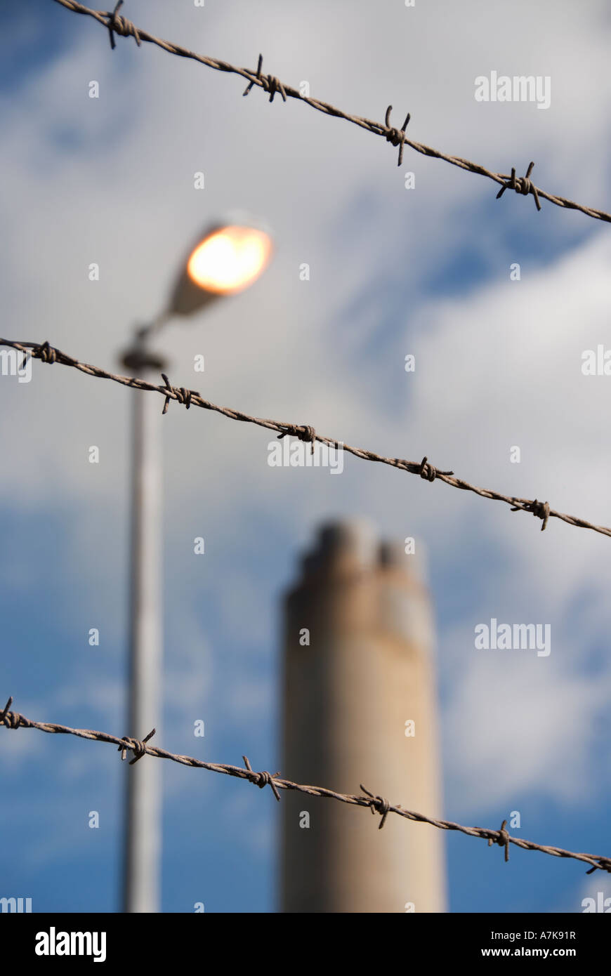 A power  station chimney with smoke shot through a barbed wire security fence. also included is a street light left on. Stock Photo