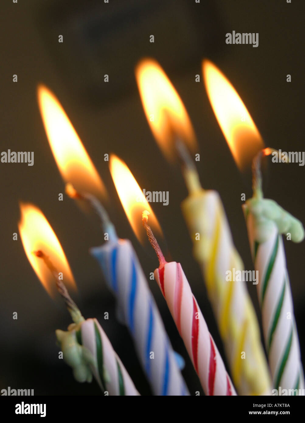 Brightly coloured striped wax birthday candles lit melting celebration
