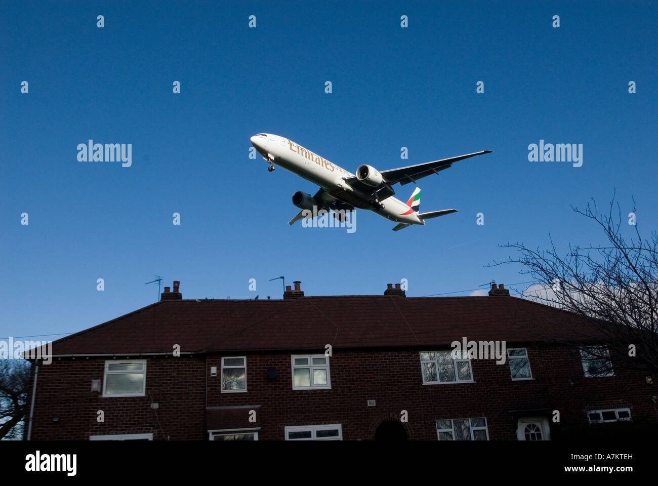 An Emirates airlines Boeing 777 300 ER landing over the rooftops of houses under the flightpath. Stock Photo