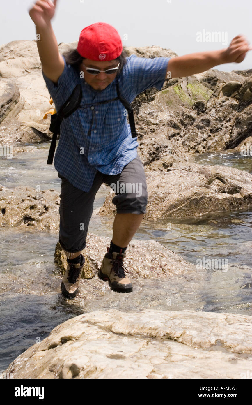 Man jumping between rocks to avoid getting wet outside Tokyo Stock