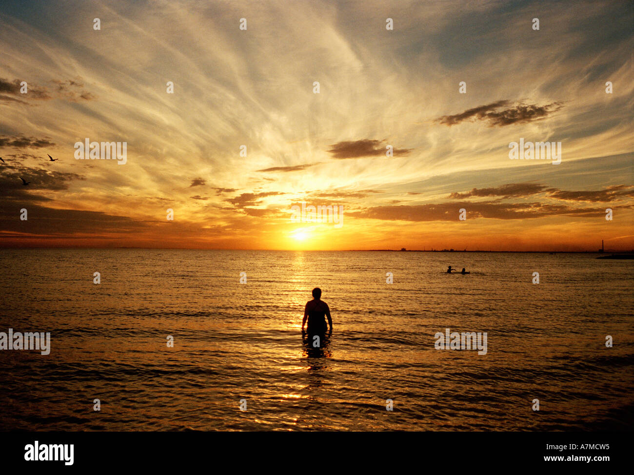 Man standing in sea at sunset Stock Photo