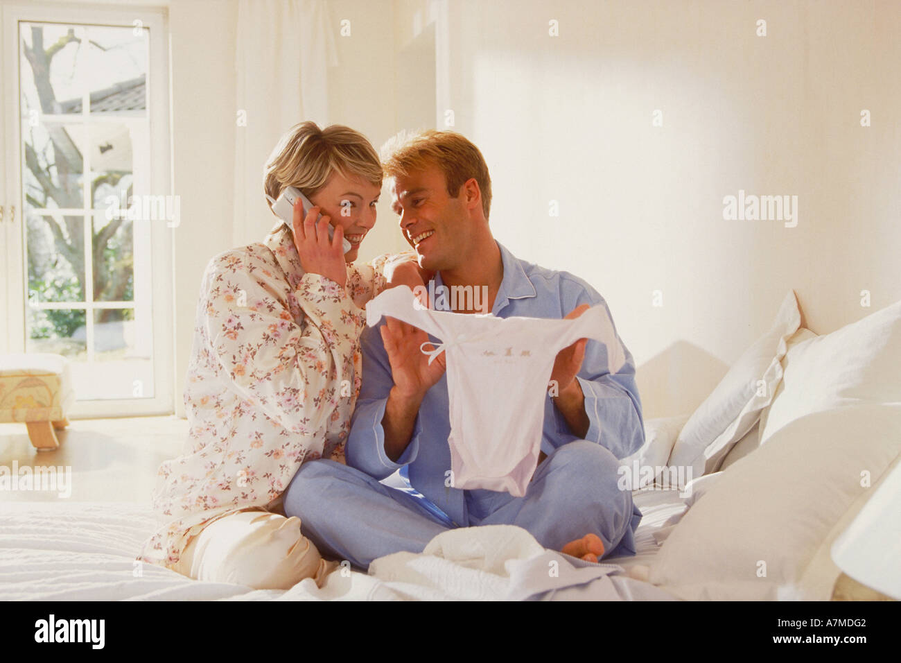 portrait of a young couple wearing pyjamas sitting in the bed with baby clothes Stock Photo