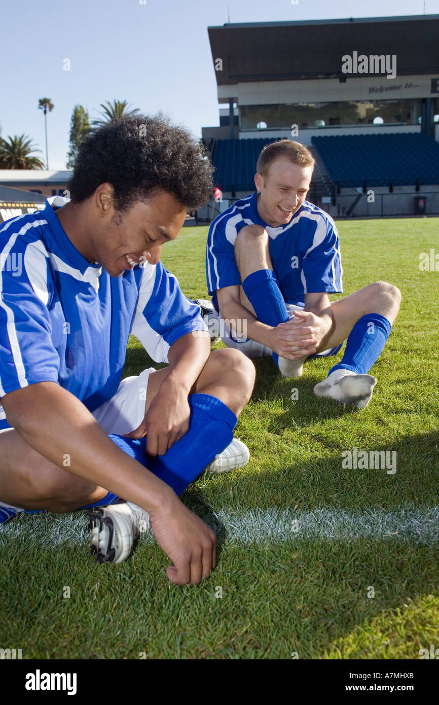 Two soccer players sitting on a soccer field laughing Stock Photo