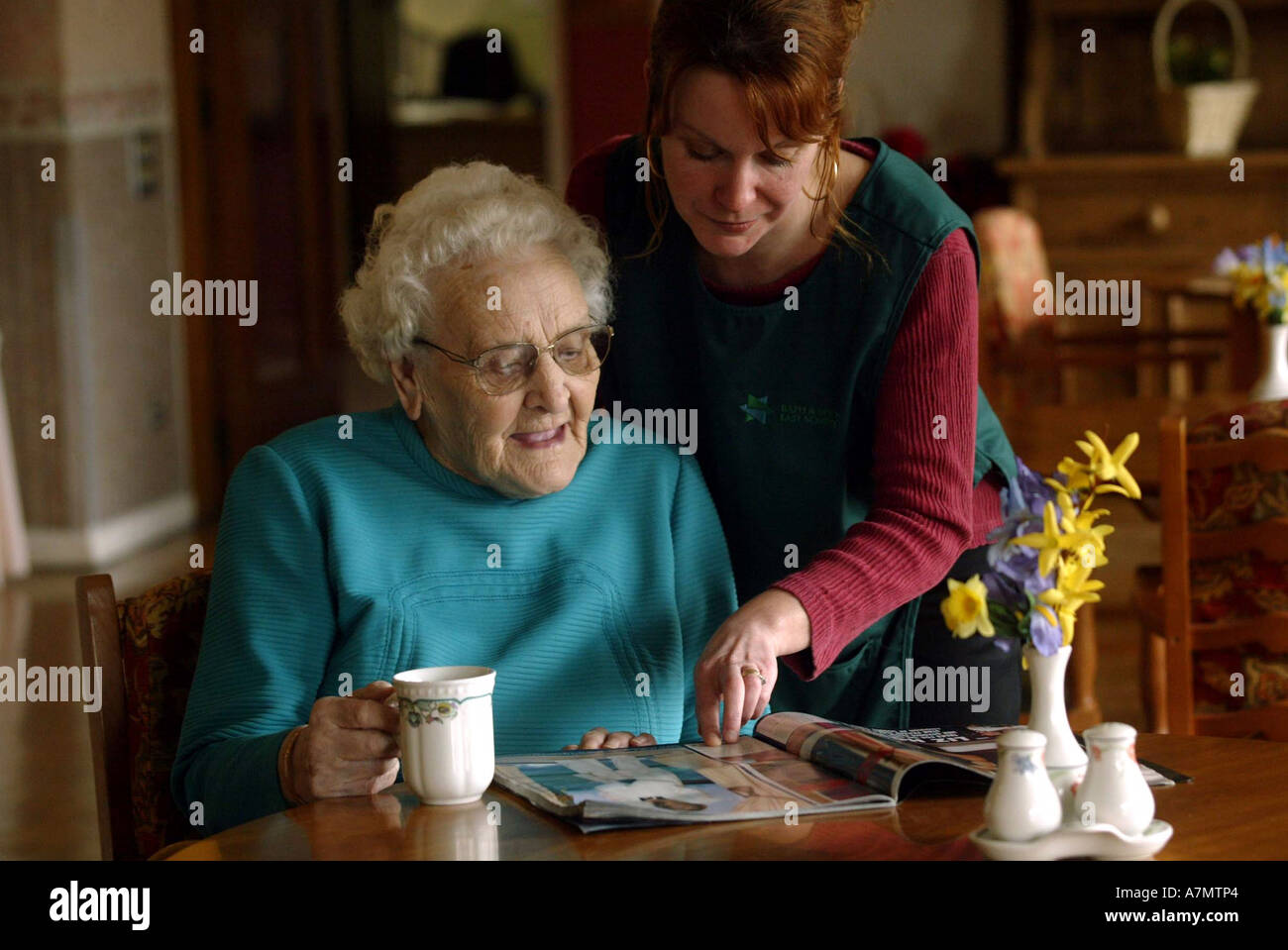 An elderly lady reads a magazine whilst talking to her carer in a old people care home. Stock Photo