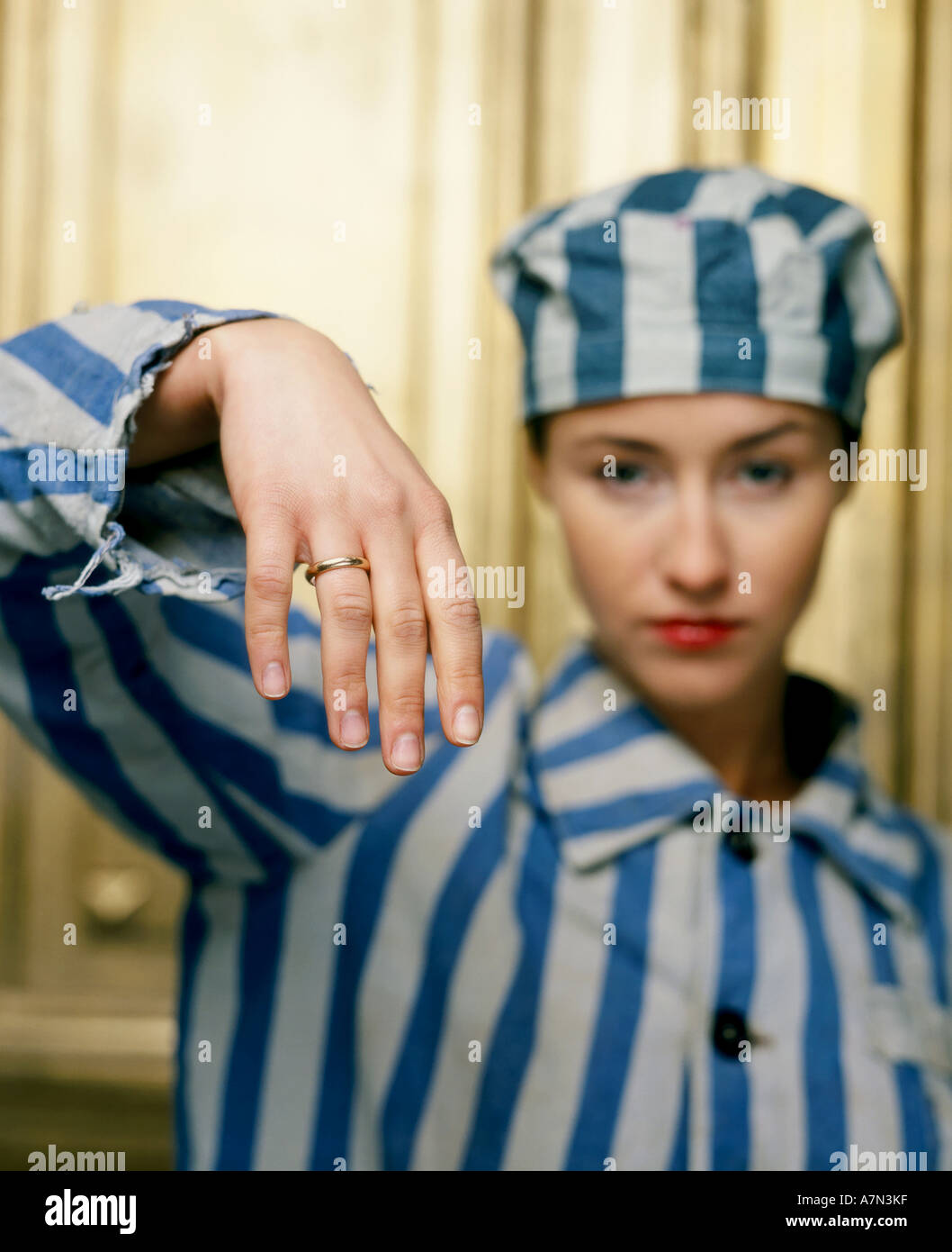 indoor studio woman young girl 20 25 dress attire jail prison shirt stripe stripes striped hat cap jewelery ring married wife Stock Photo