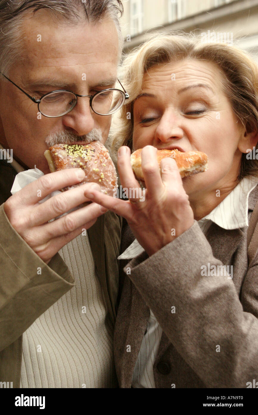 woman man 45 50 mature couple blond blonde white hair beard glasses jacket cuddle eat eating cuddle cuddles cake cakes doughn Stock Photo