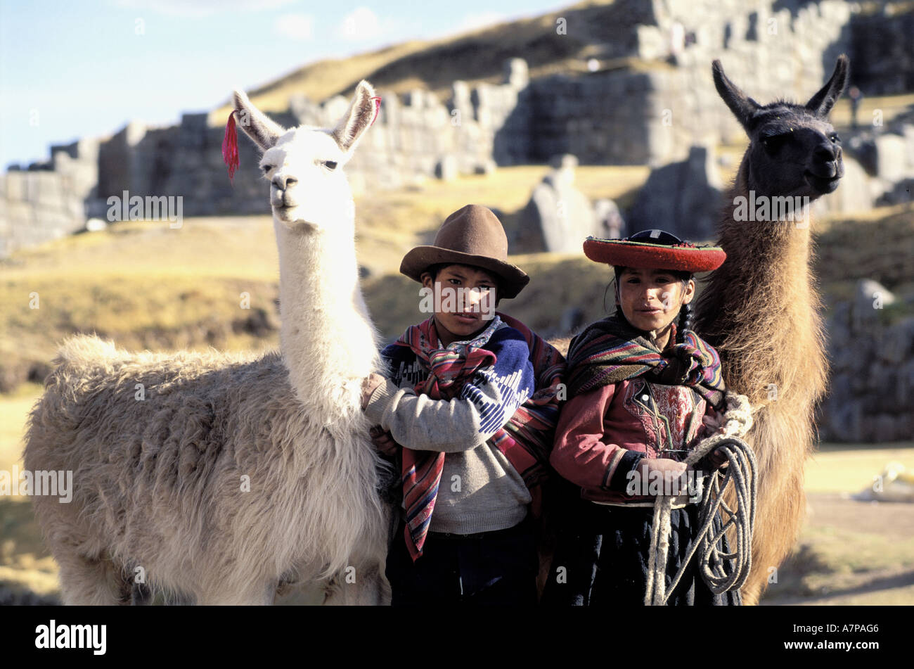 Peru, Cuzco Department, young children and their llamas in front of the Inca fortress of Sacsayhuaman Stock Photo