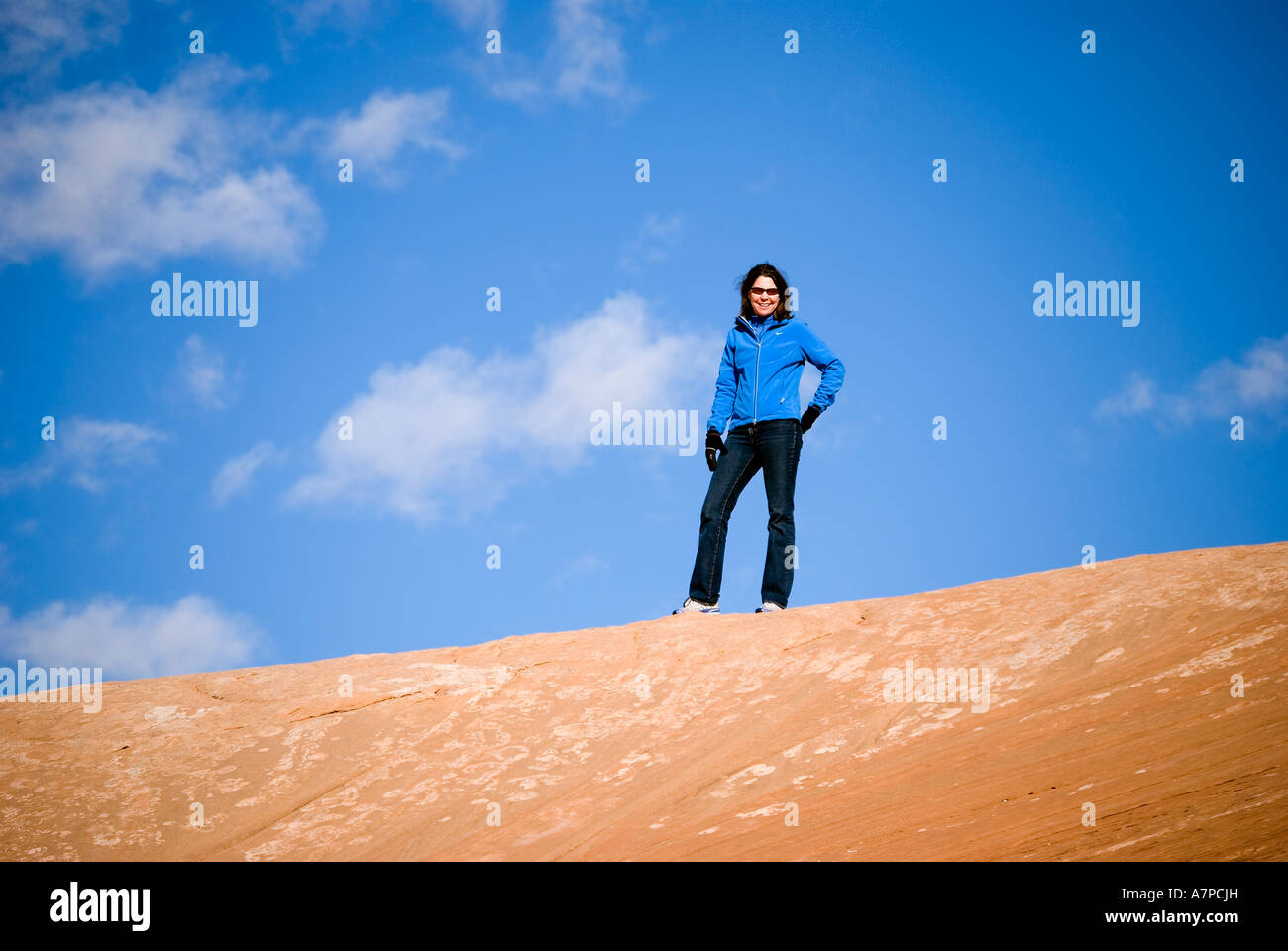 Smiling woman hiker standing on Entrada sandstone ridge with blue sky and white clouds Arches National Park Utah USA Stock Photo