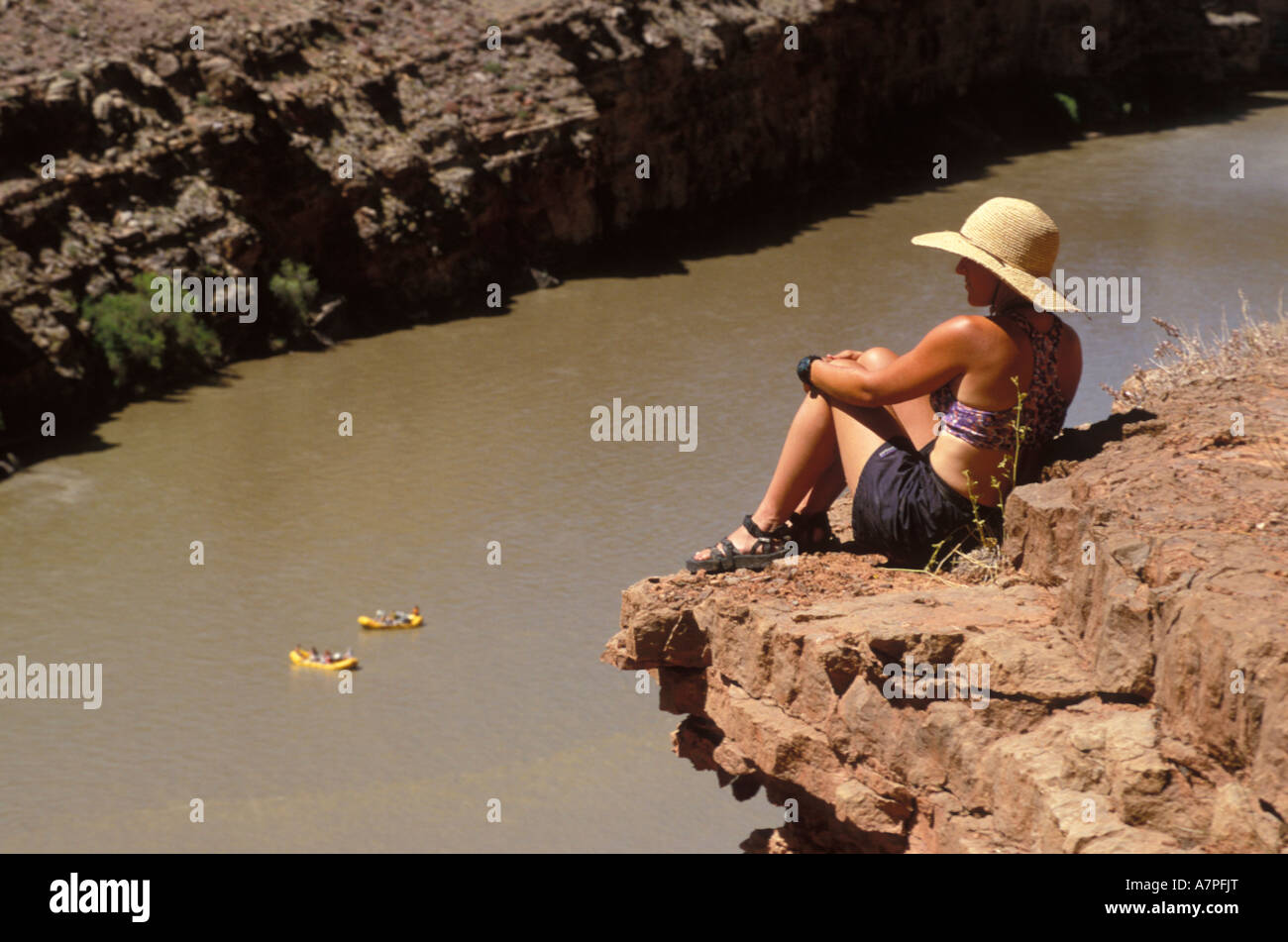 Female hiker sitting on an out rocky outcrop overlooking two rafts meandering down the Colorado River Utah USA Stock Photo