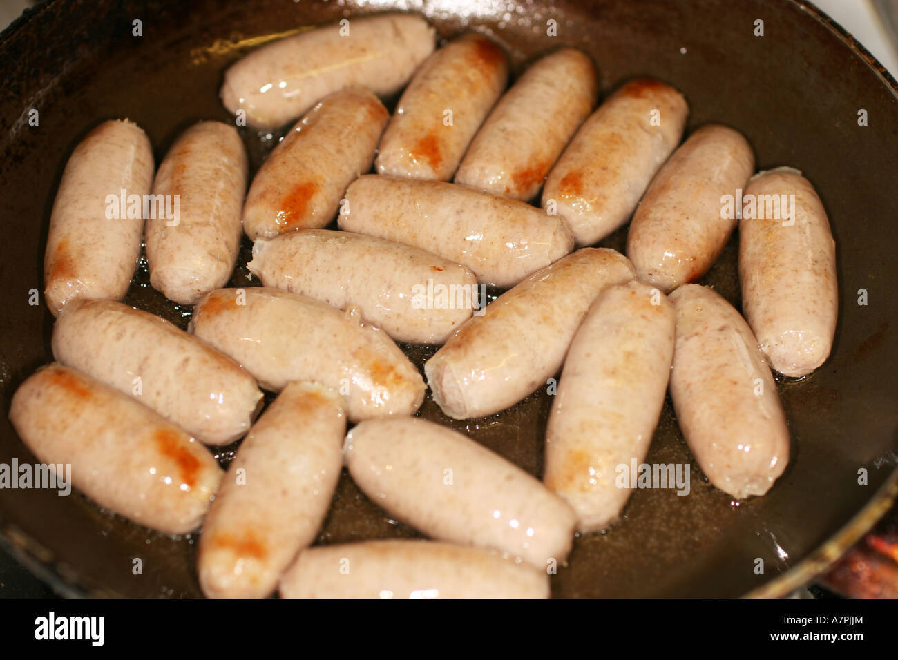 Small cocktail sausages cooking in a frying pan. Stock Photo