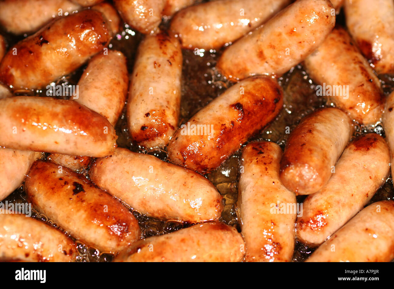 Small cocktail sausages cooking in a frying pan. Stock Photo