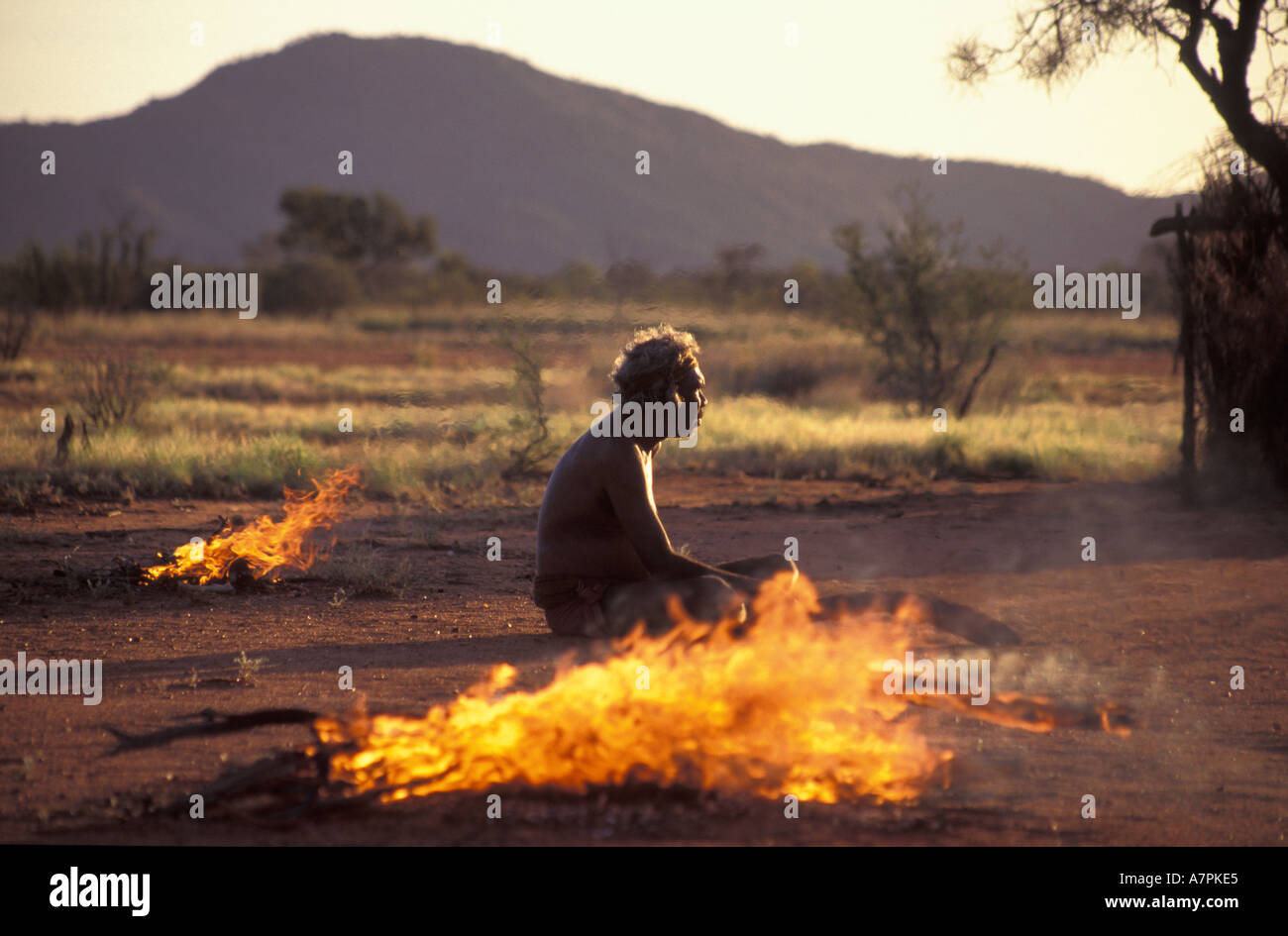 Aboriginal clan elder sits beside fires to deter mosquitoes flies at sunset in his remote desert homeland in Central Australia Stock Photo