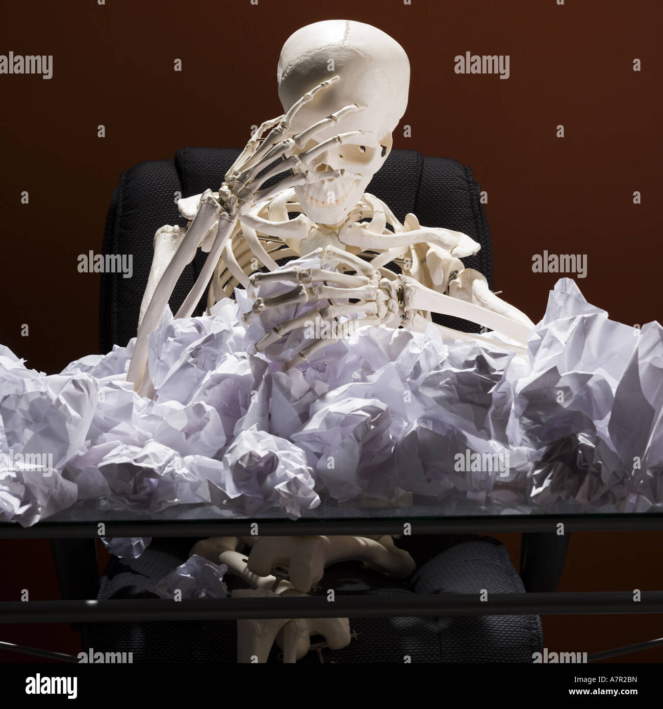 Skeleton Sitting At Desk With Crumpled Papers Stock Photo