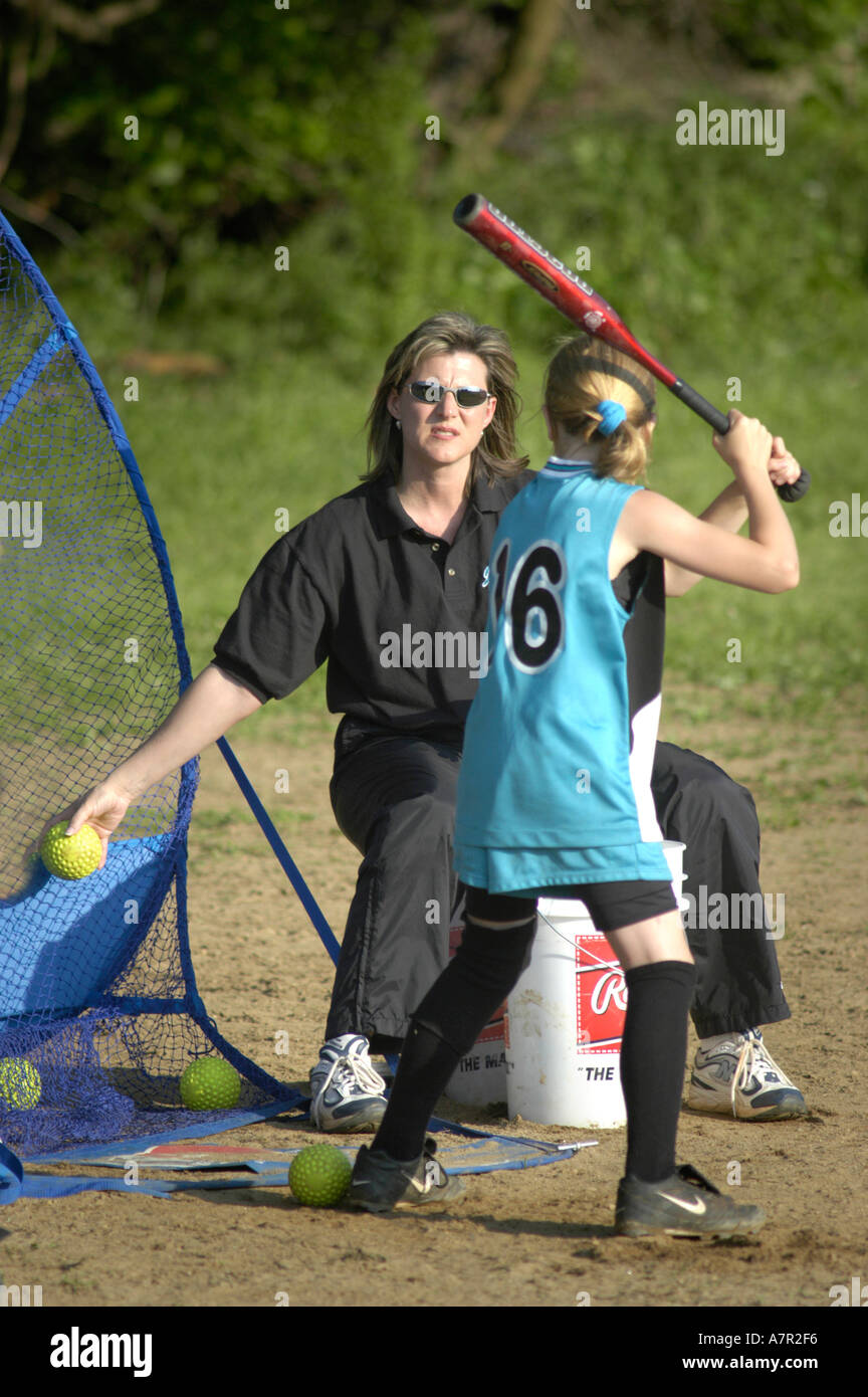 Girls learning to hit softball with coaches and practice net in