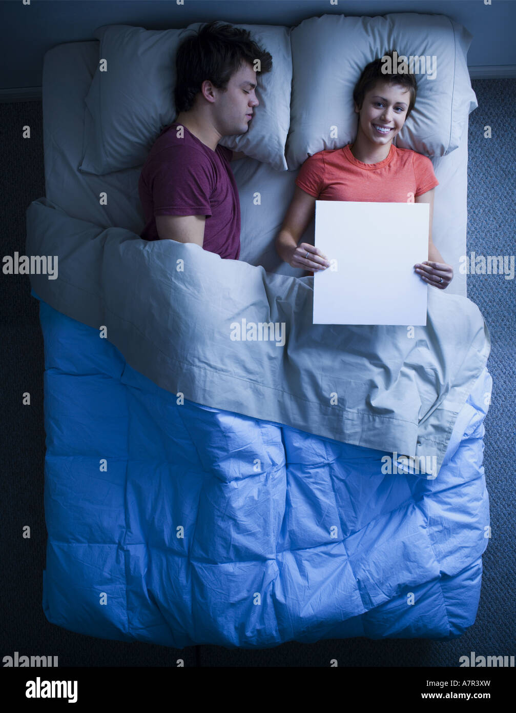 Man asleep in bed and woman holding blank sign smiling Stock Photo