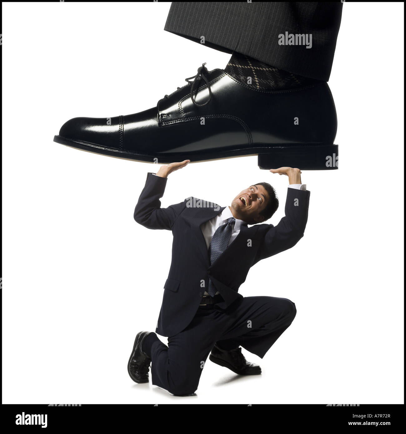 Businessman kneeling and holding up large dress shoe Stock Photo