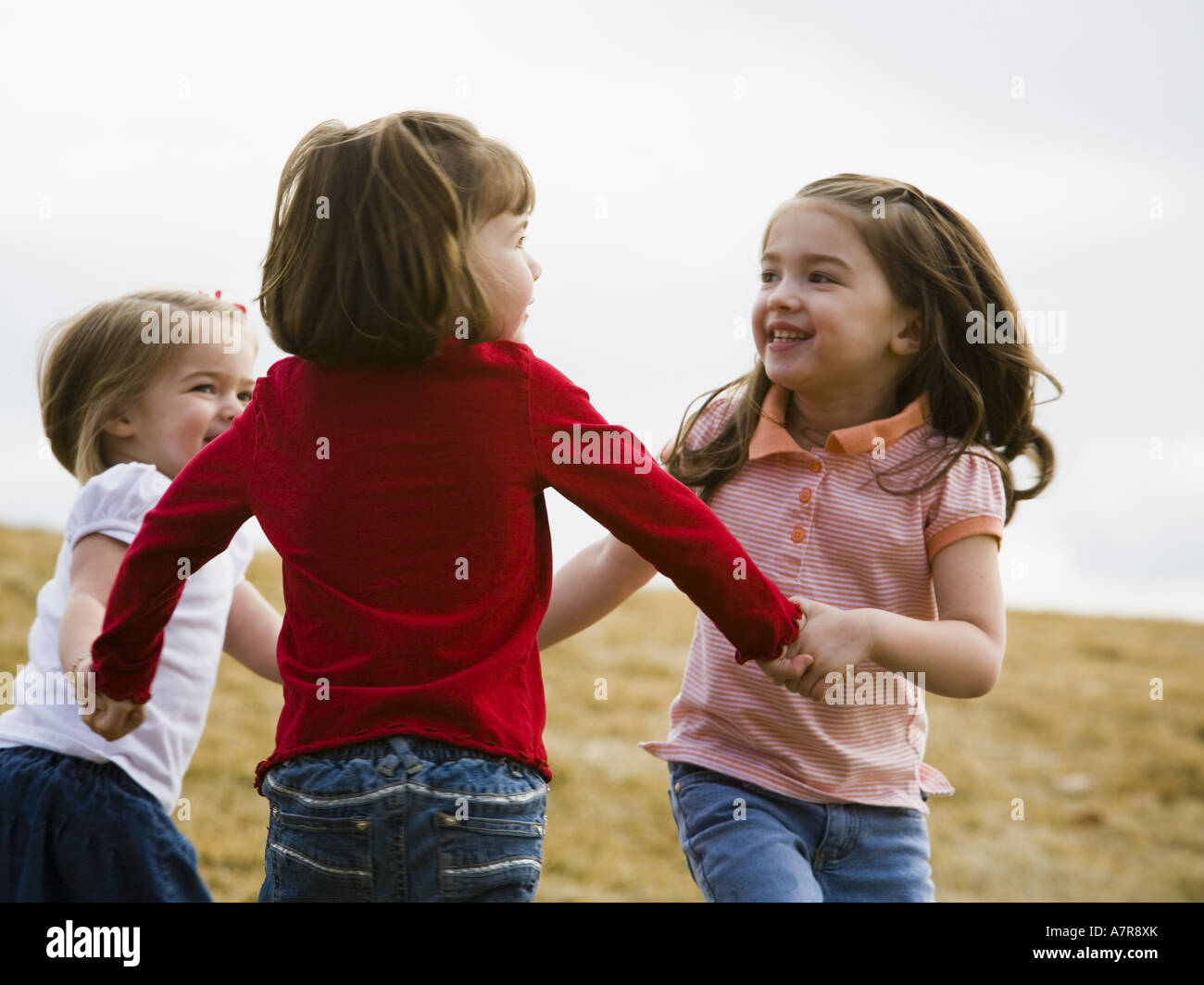 Three girls playing and holding hands outdoors Stock Photo - Alamy