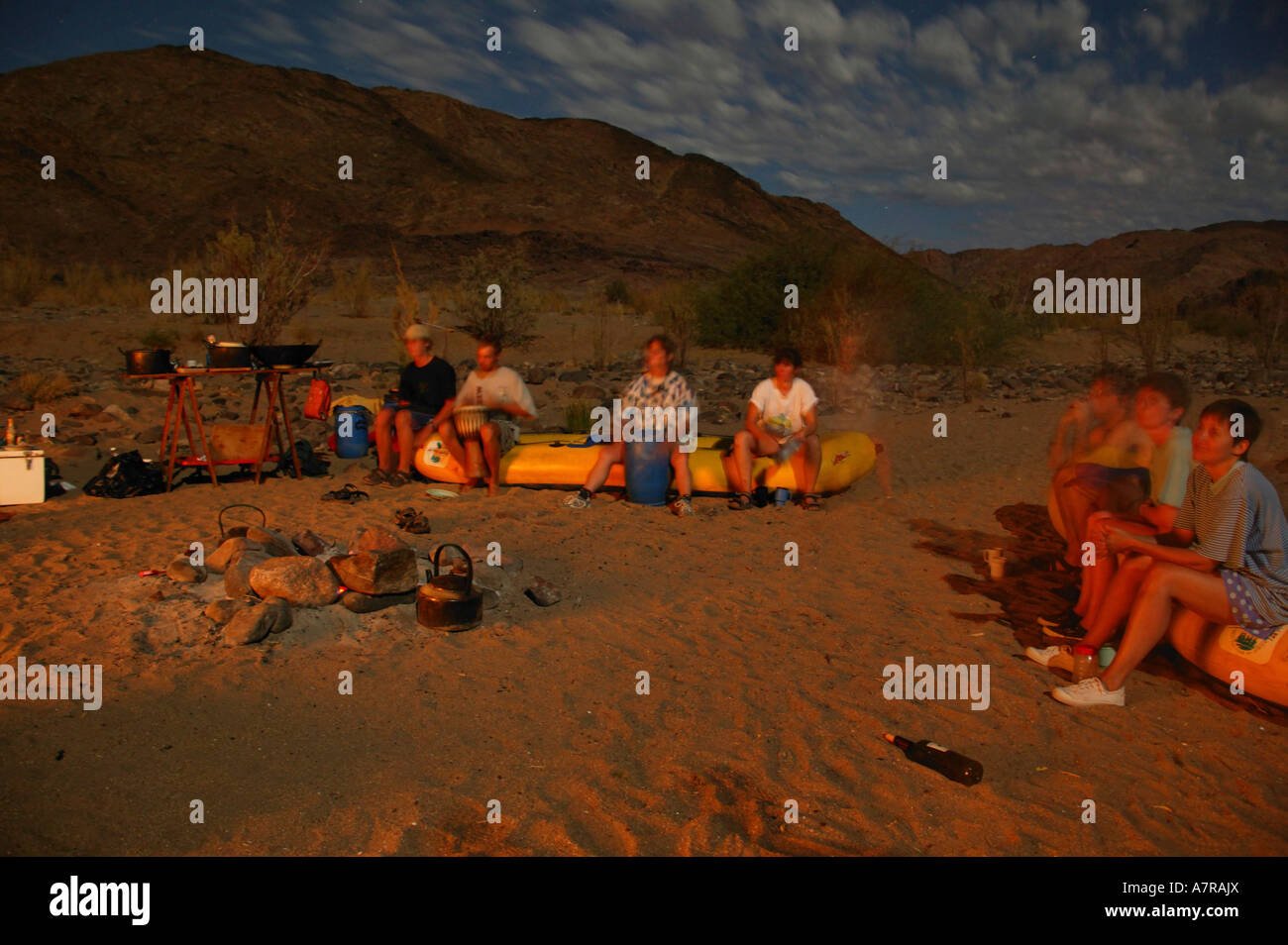 A moonlit photograph of campers relaxing at the fireside while on a canoeing trip on the Orange River in the Richtersveld Stock Photo