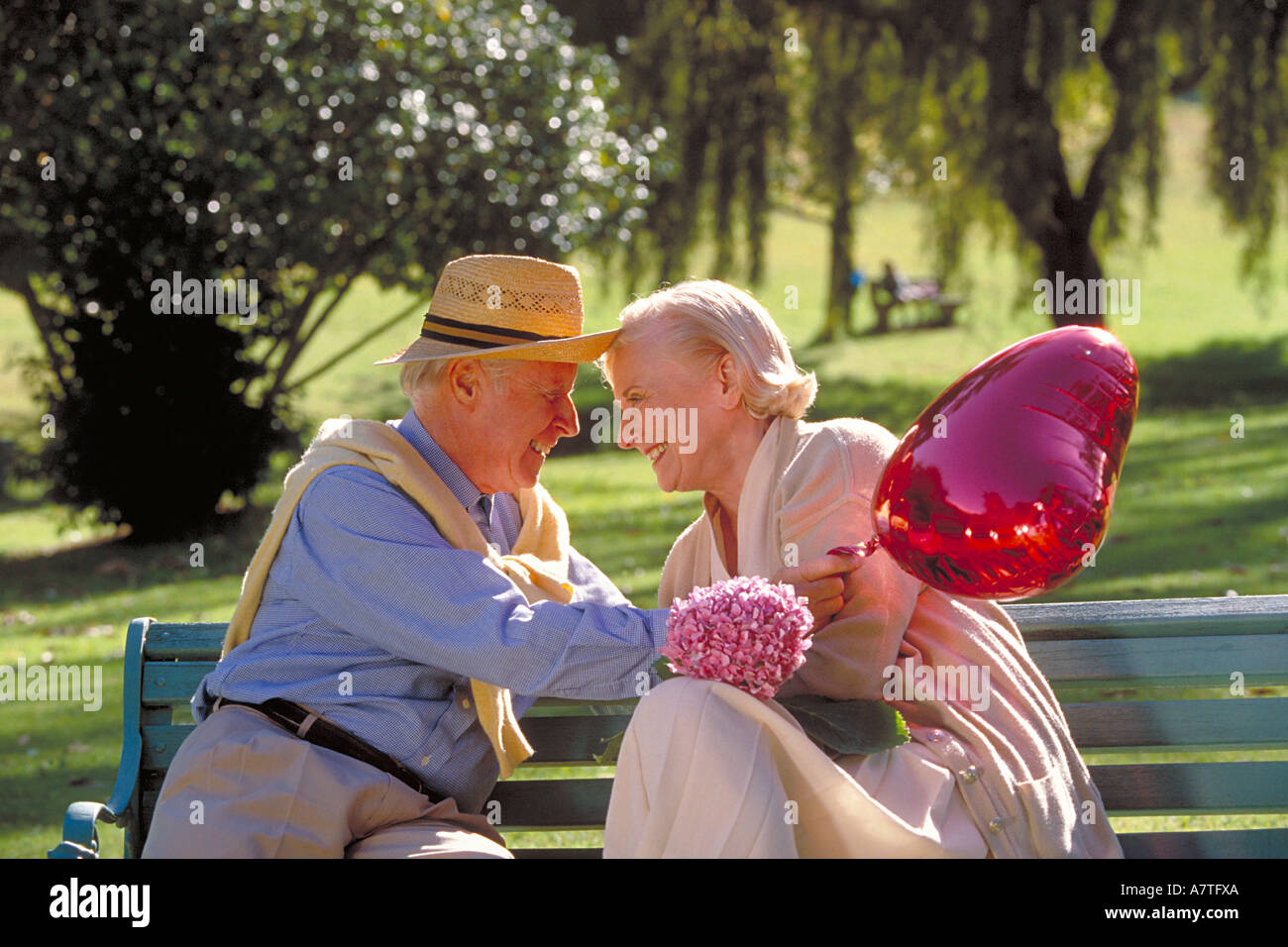 portrait of elderly couple sitting on a bench in a park with a red ...