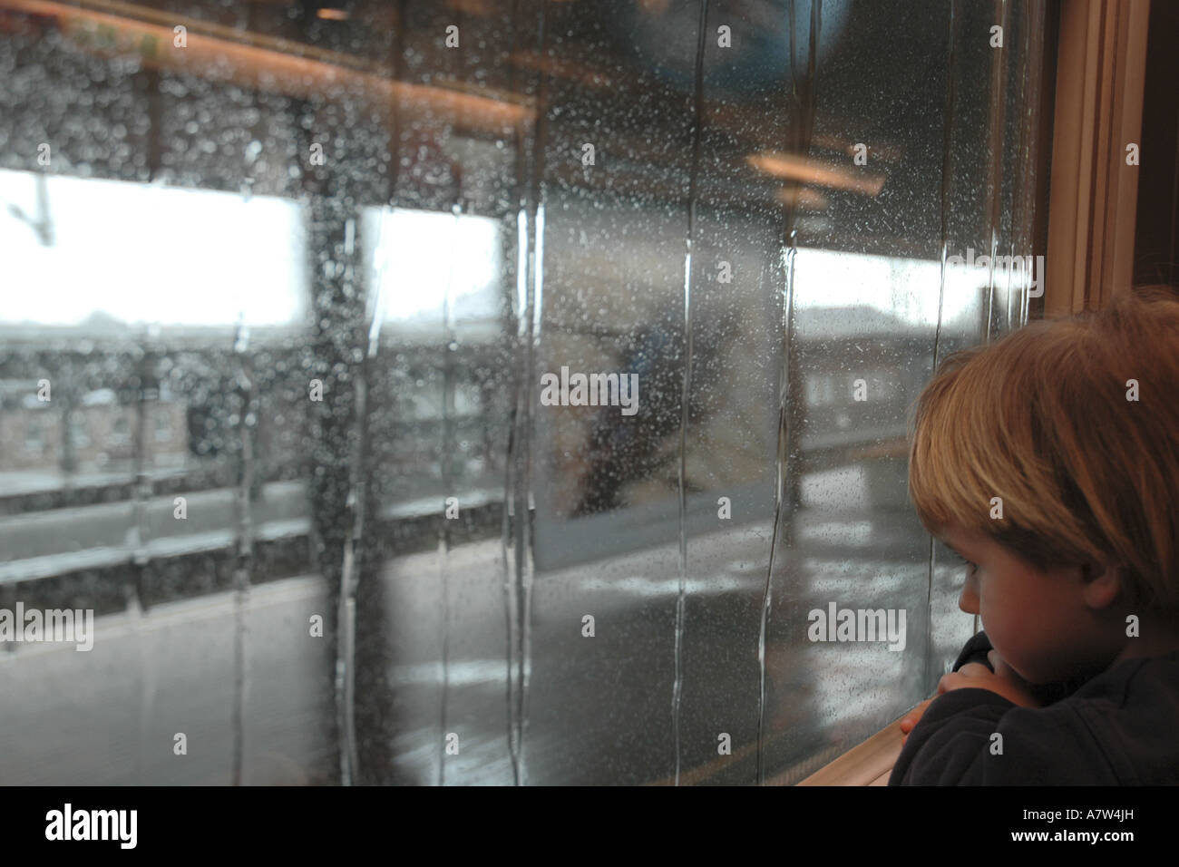 boy in front of window pane wet from rain in a railway building, Germany, Hesse, Frankfurt am Main Stock Photo