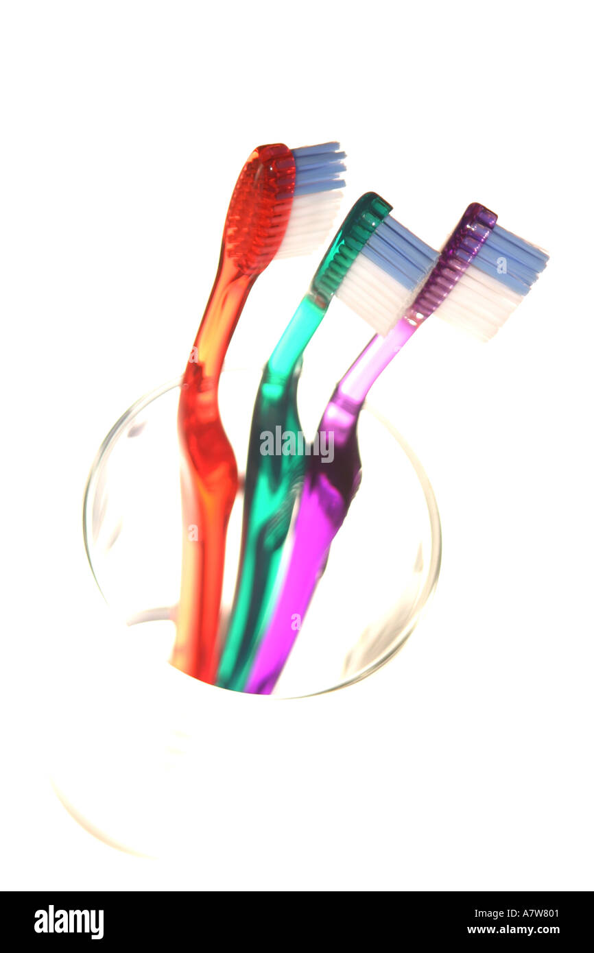Clear coloured toothbrushes in a clear glass with a bright white background Stock Photo