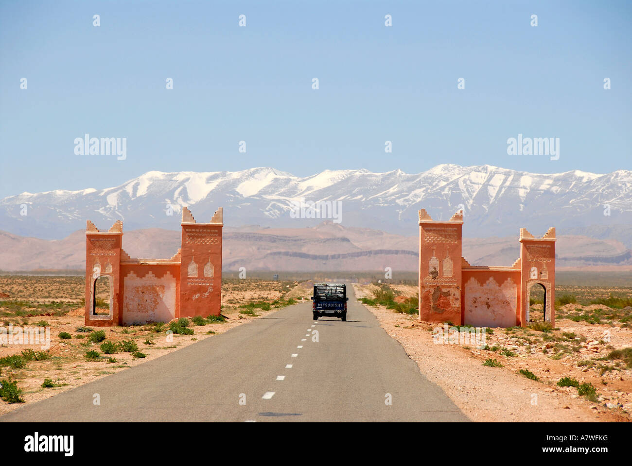 Car drives on straight street through a gate towards snowcapped mountains of the High Atlas between Tinerhir and Boumalne-du-Da Stock Photo