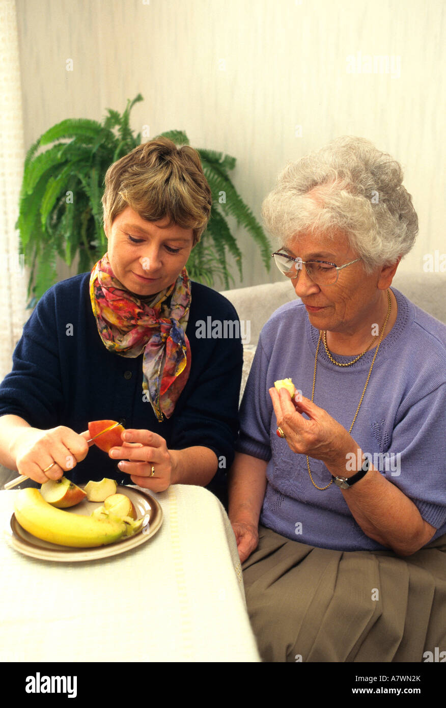 Woman is cutting fruits in small pieces for female senior Stock Photo