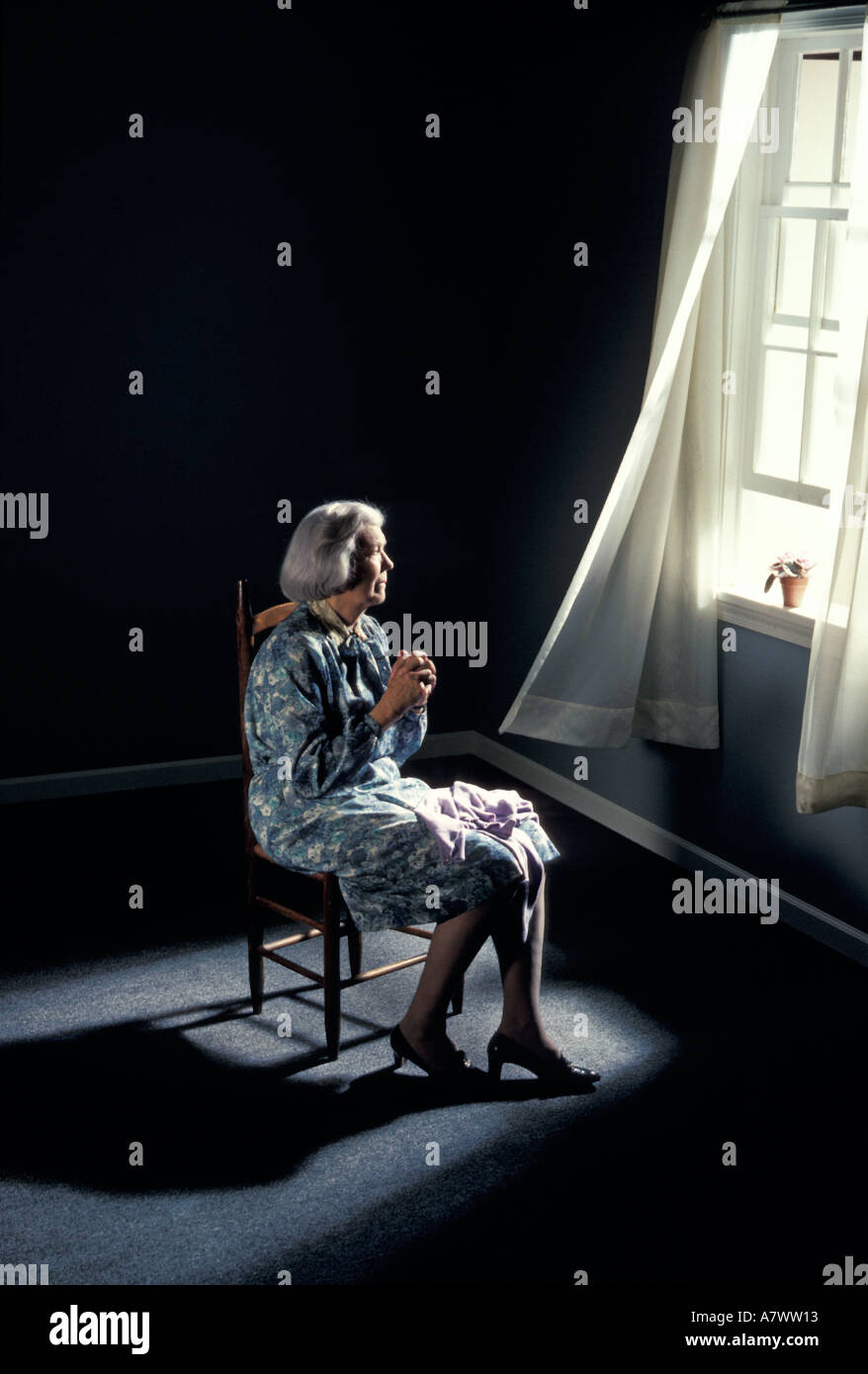 depressed lonely elderly woman by window squander waste dissipate ravage misuse desecrate devastate widow retirement abuse Stock Photo