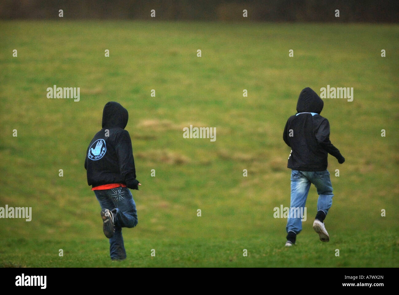 TWO YOUNG MALES WEARING HOODED TOPS RUN ACROSS A FIELD UK Stock Photo