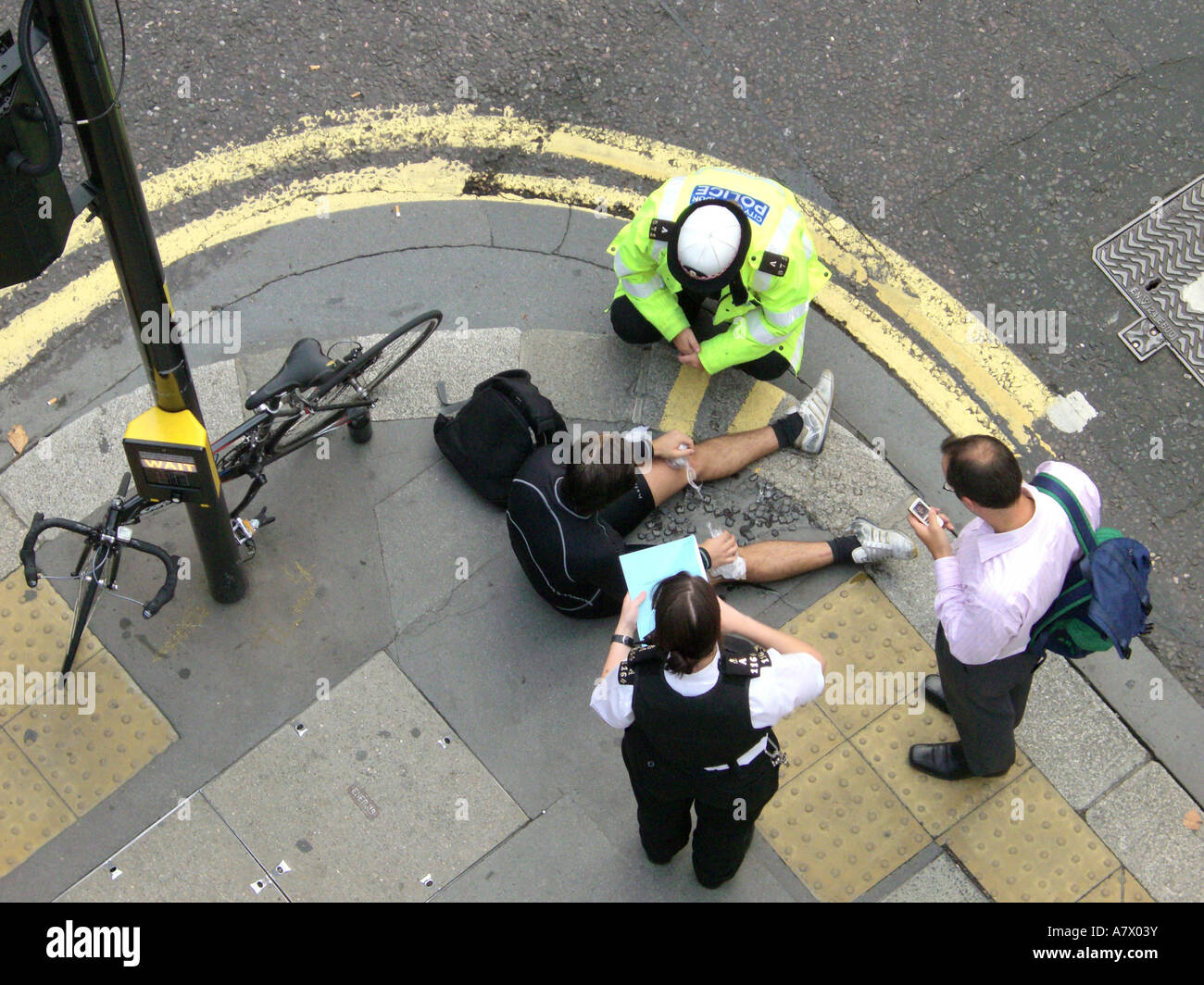 Cyclist lying on pavement with police officer and witness after accident on City of London Street Stock Photo