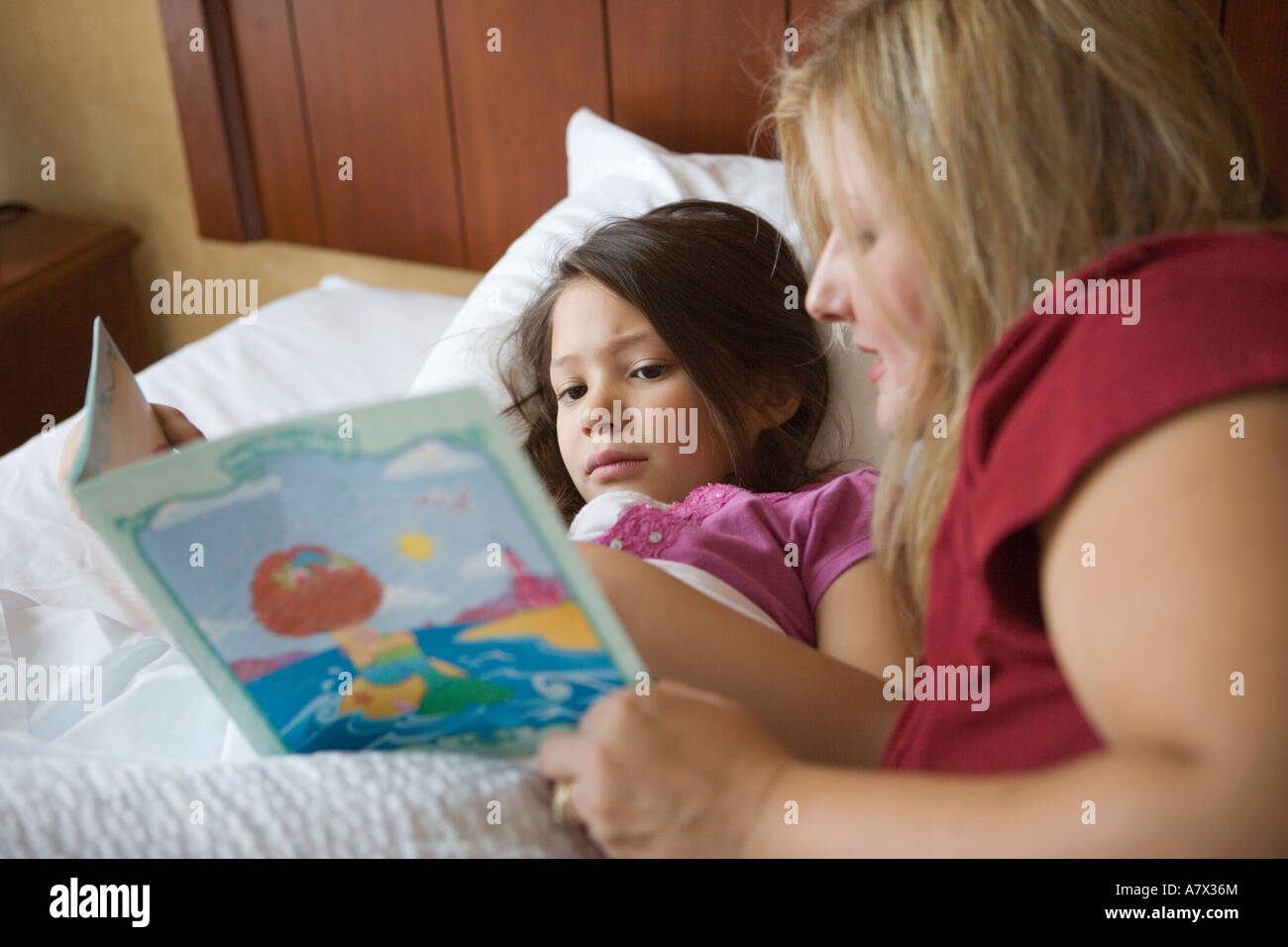 mother reading bed time story to her six year old daughter at home sick child care caring for parenting parent mom child book Stock Photo