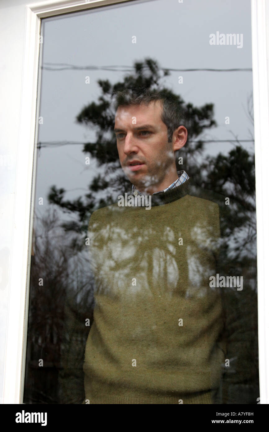 Man staring out of glass door showing reflection of trees Stock Photo