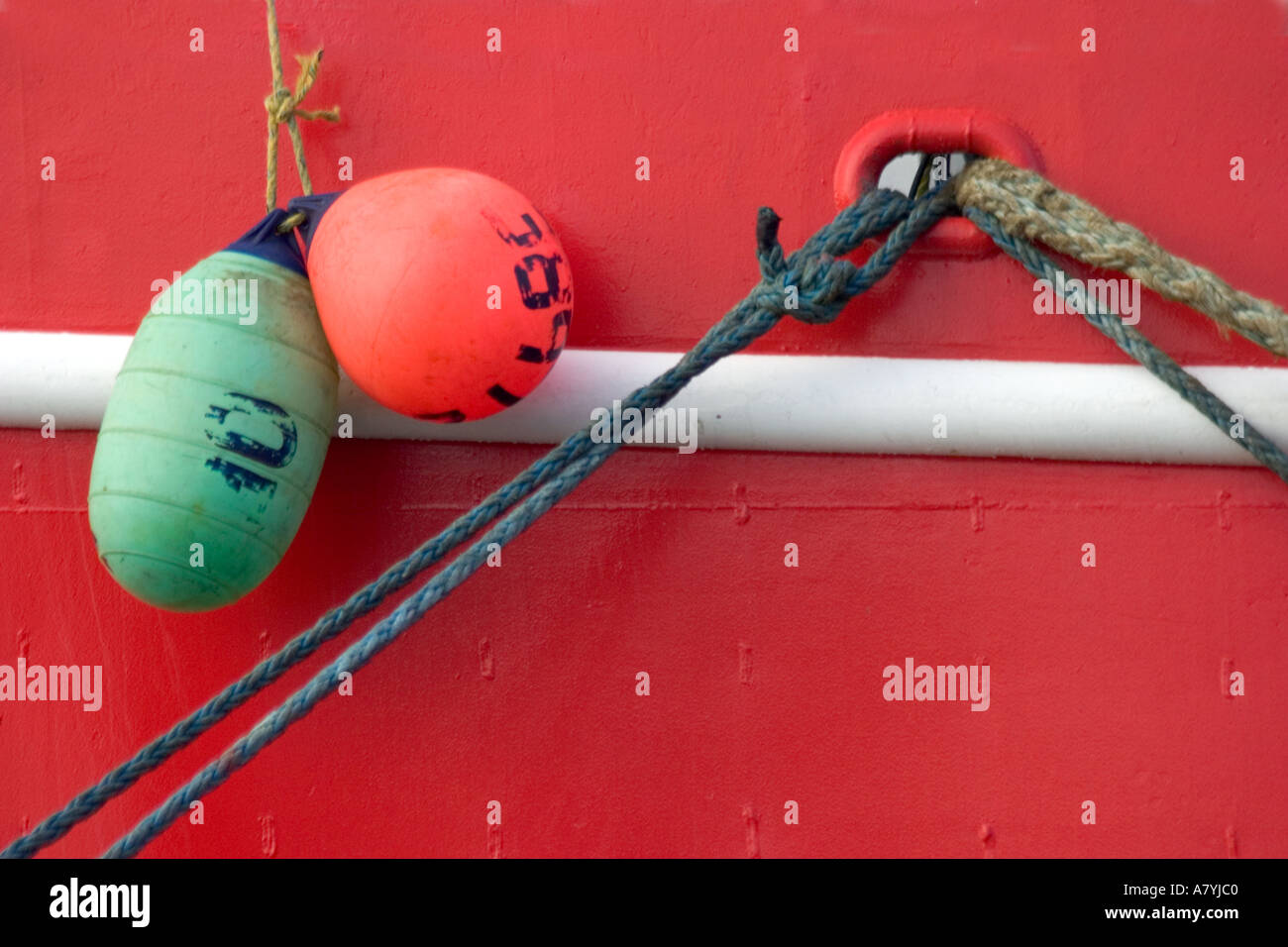 Two fenders or bumpers hang from the side of a red fishing boat Stock