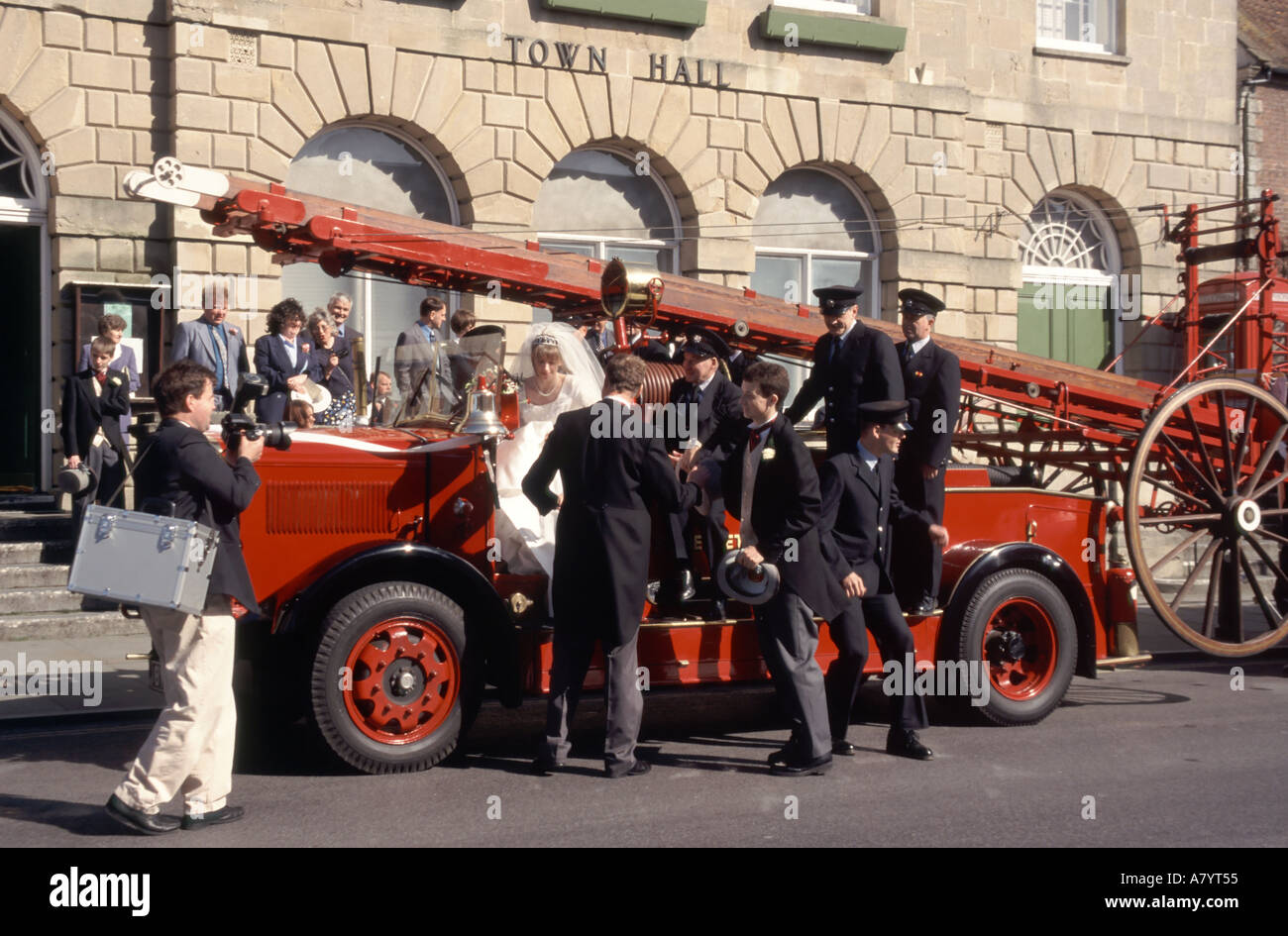 Glastonbury wedding guests on and around restored old fashioned fire engine parked outside town hall photographer attending Somerset England UK Stock Photo