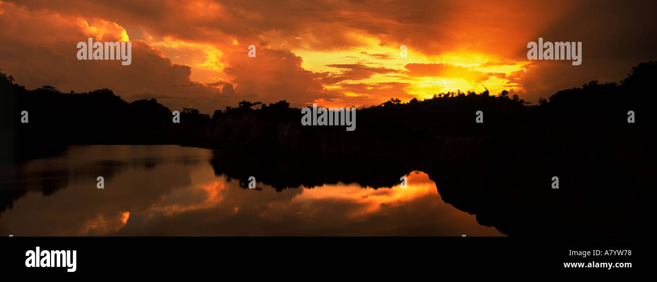 Silhouette of African bush & trees against orange yellow sky of sunset as sun is setting just before dark on lake  and edge of rainforest, West Africa Stock Photo