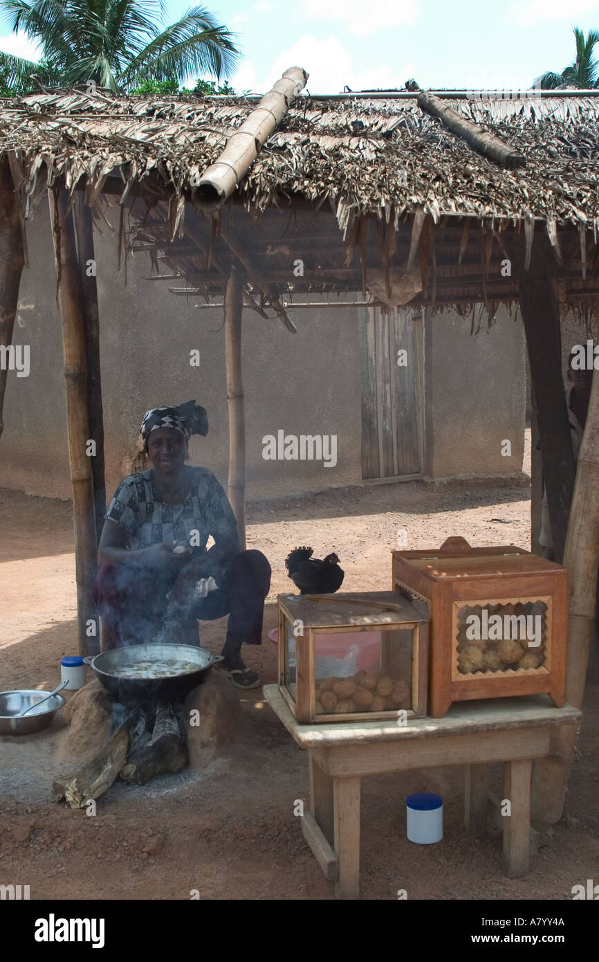 West African village woman food vendor cooking over charcoal fire in street market stall in Ghana West Africa Stock Photo