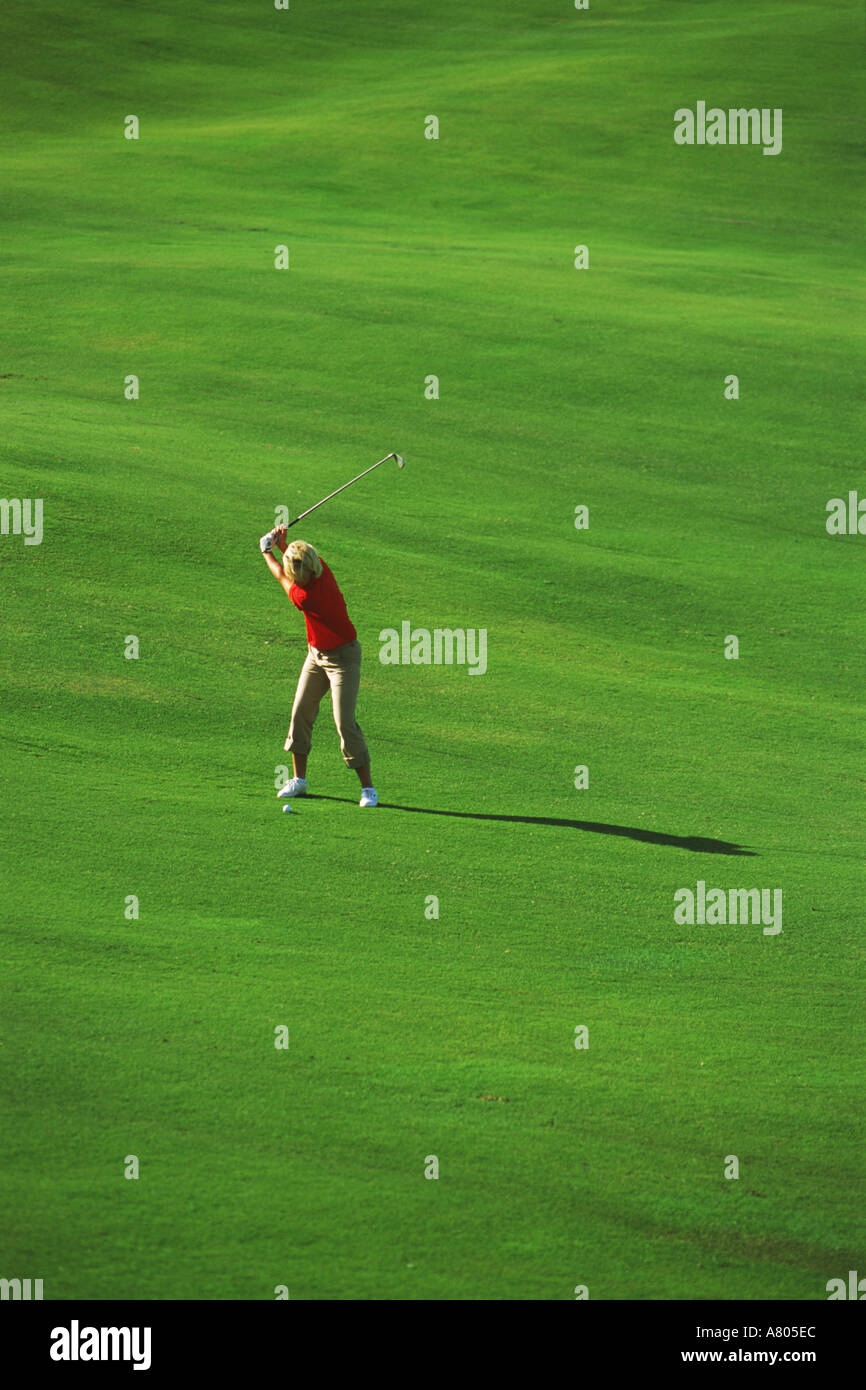 Woman with perfect form hitting iron shot off lush green fairway Stock
