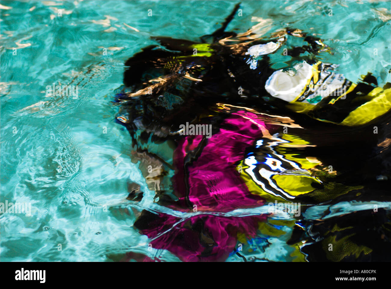 Abstract scuba diver with colourful drysuit swimming underwater in pool seen from surface Stock Photo